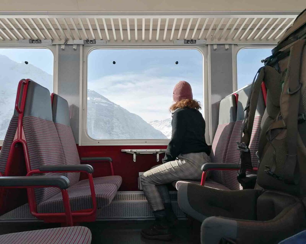 Interrail Reservierungen Frau schaut aus dem Zugfenster auf Berge